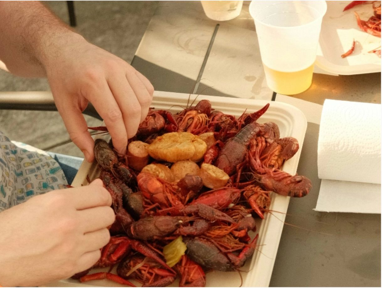 Two people eating trays of crawfish, sausage, and potatoes at a picnic table at the SPE Crawfish Boil.